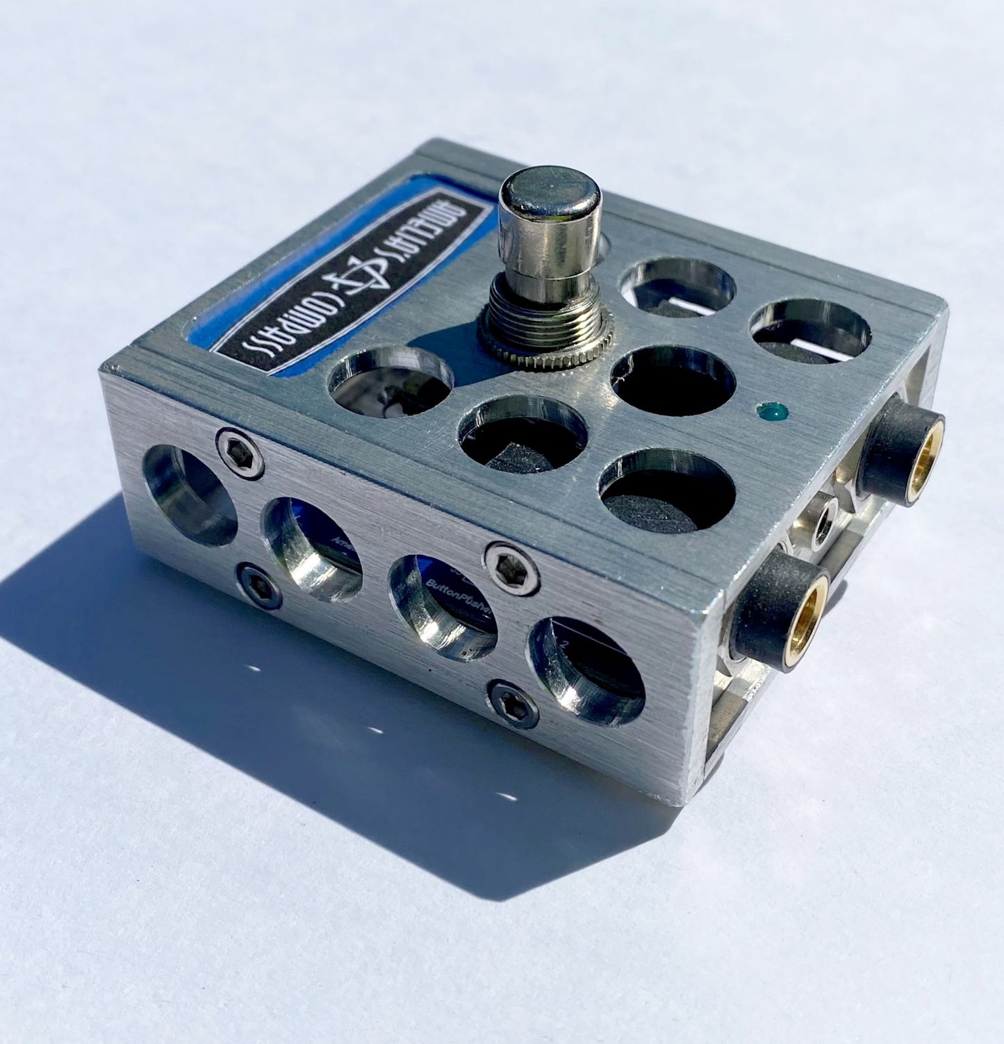 A metal foot switch with multiple input jacks and a central button, with the brand 'Amelia's Compass' visible on the top surface.