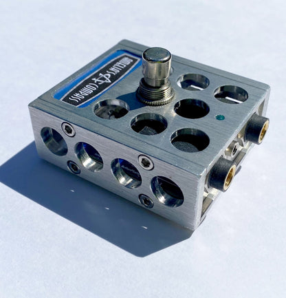 A metal foot switch with multiple input jacks and a central button, with the brand 'Amelia's Compass' visible on the top surface.