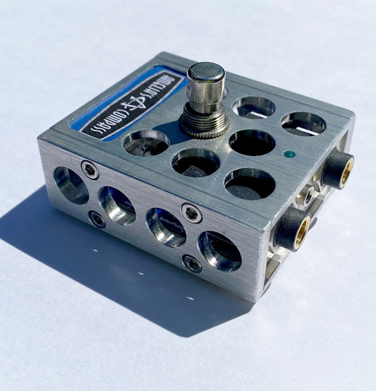 A metal foot switch with multiple input jacks and a central button, with the brand 'Amelia's Compass' visible on the top surface.