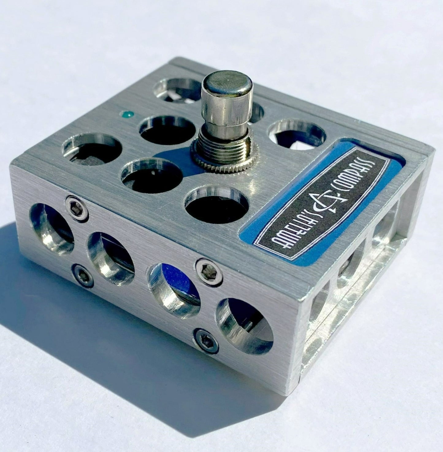 A metal foot switch with multiple input jacks and a central button, with the brand 'Amelia's Compass' visible on the top surface.