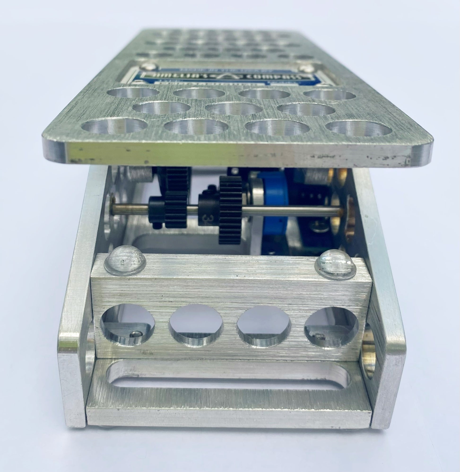 An aluminum PedalPusher expression pedal, featuring multiple holes on the top surface and a blue label in the center.